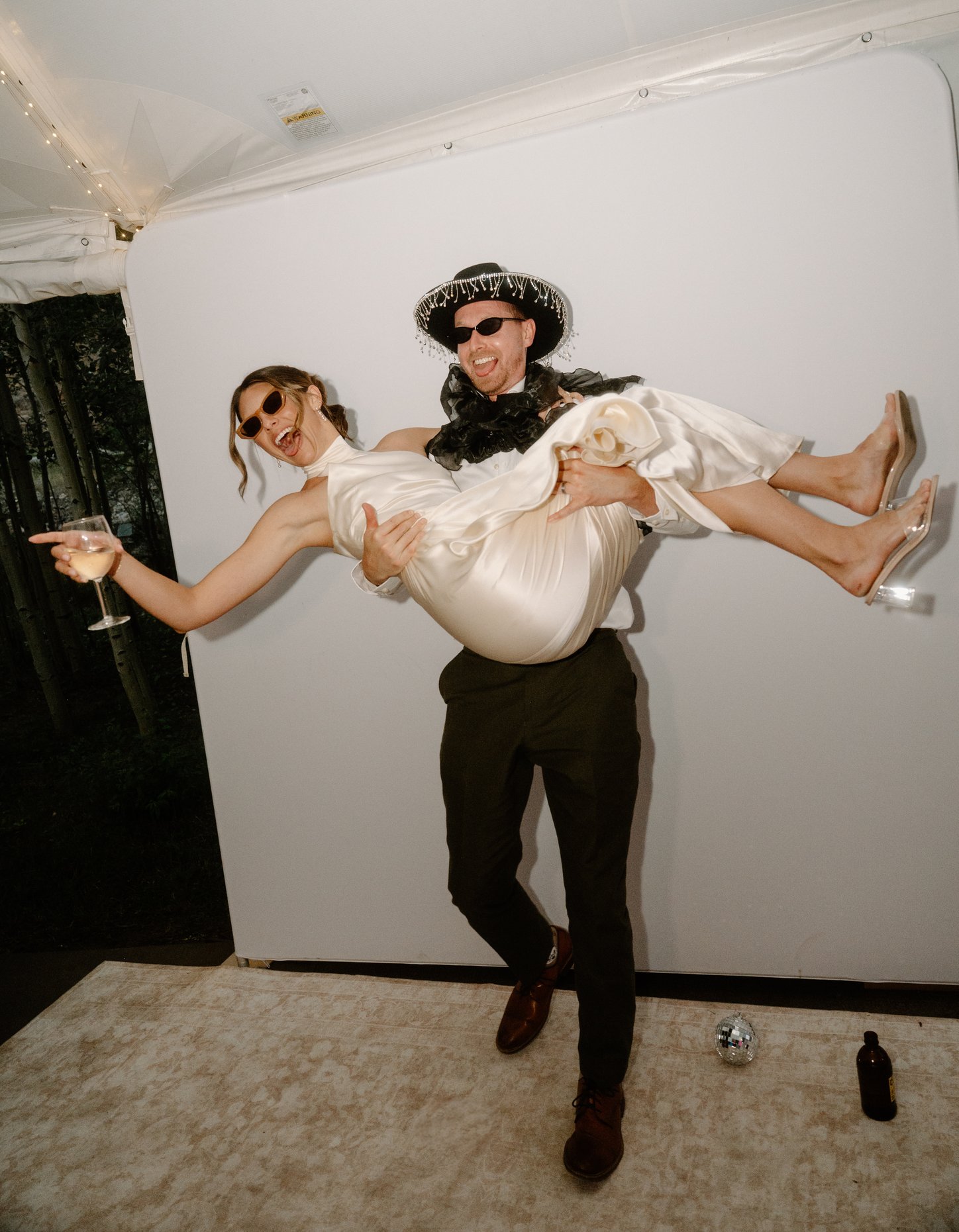 A man in a hat carrying a woman in a white dress in front of the booth backdrop