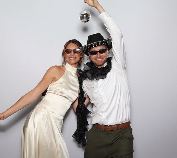 Two people in a photo booth, woman in cream dress, man holding disco ball
