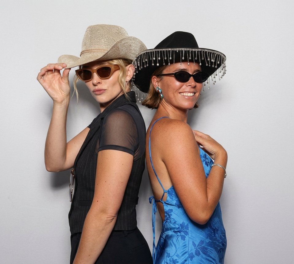 Two guests posing back to back at the booth in cowboy hats and sunglasses