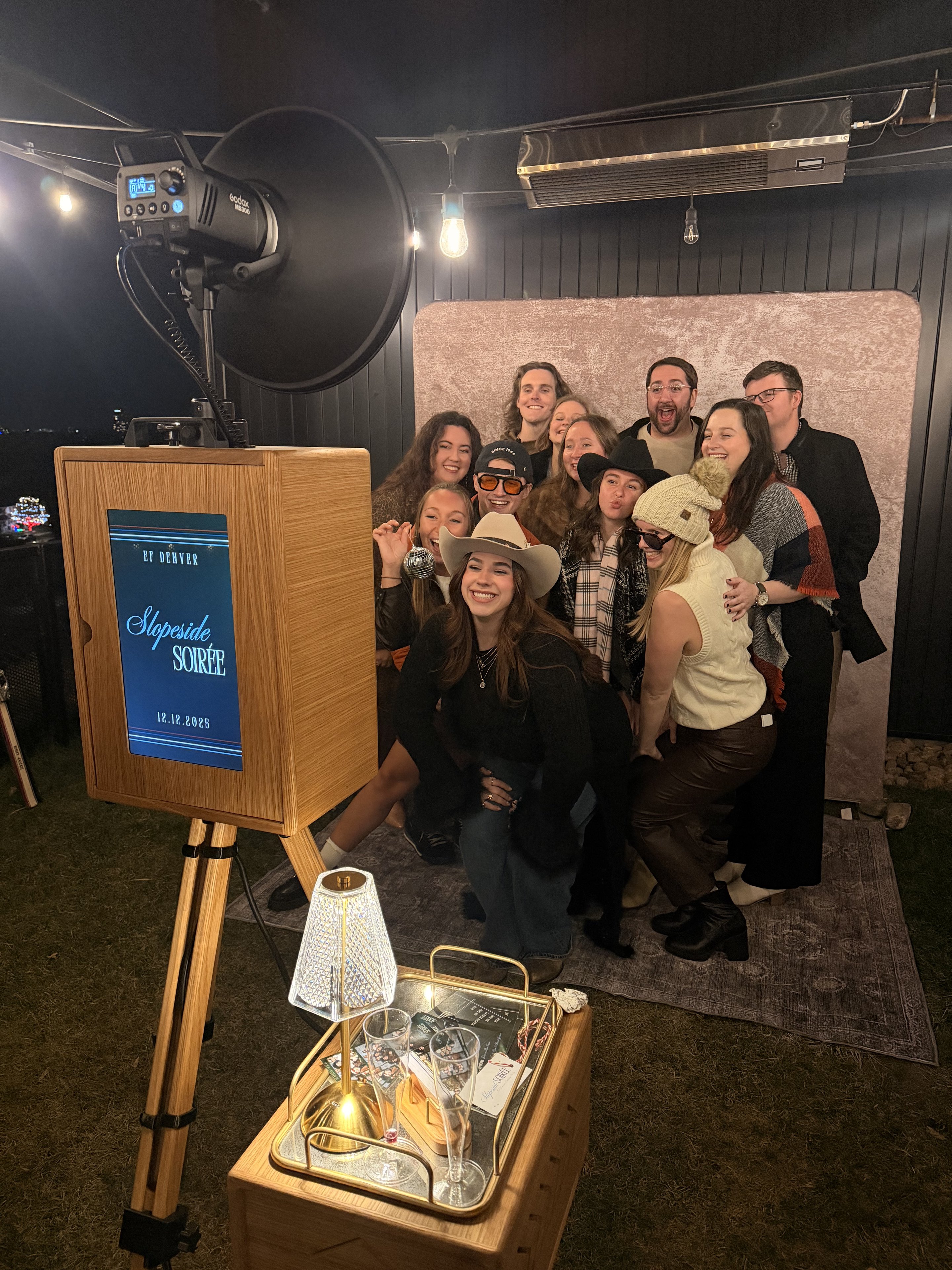 A group of guests posing in front of the booth backdrop at an evening corporate party