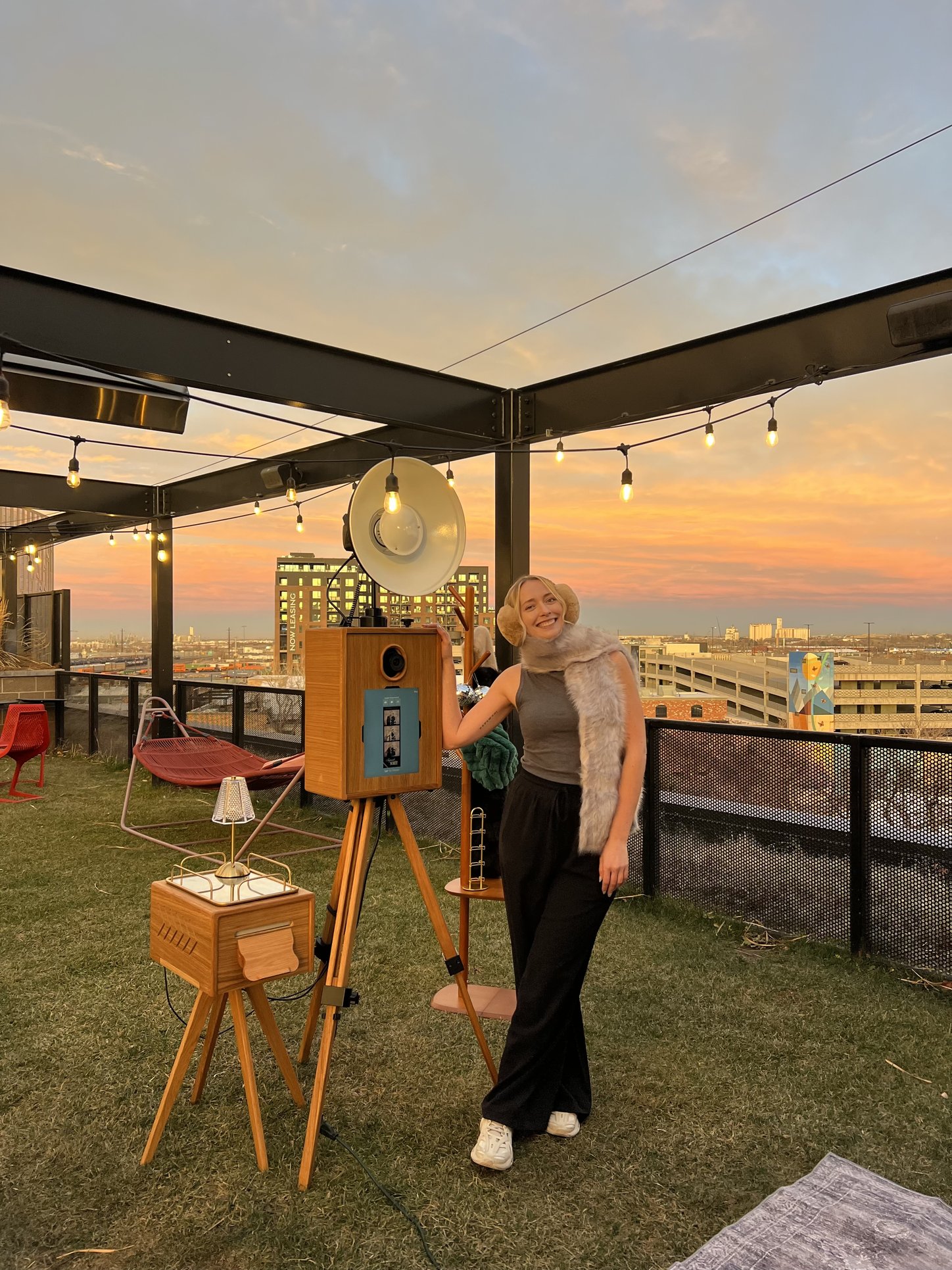 Ashley beside the booth on a rooftop at sunset