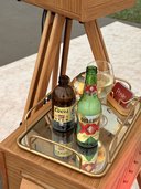 A mirrored tray on a wooden tripod table, two bottles and a wine glass